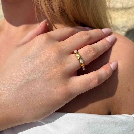 Close-up of a hand wearing a gold ring with pearls on a blurred background