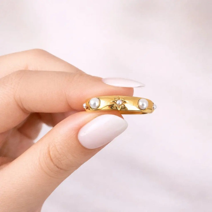 Gold ring with pearls held by a hand on a light pink background