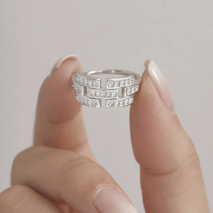 Silver ring with diamonds held between fingers against a neutral background