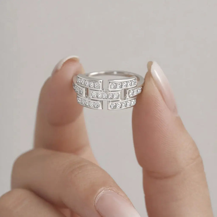 Silver ring with diamonds held between fingers against a neutral background