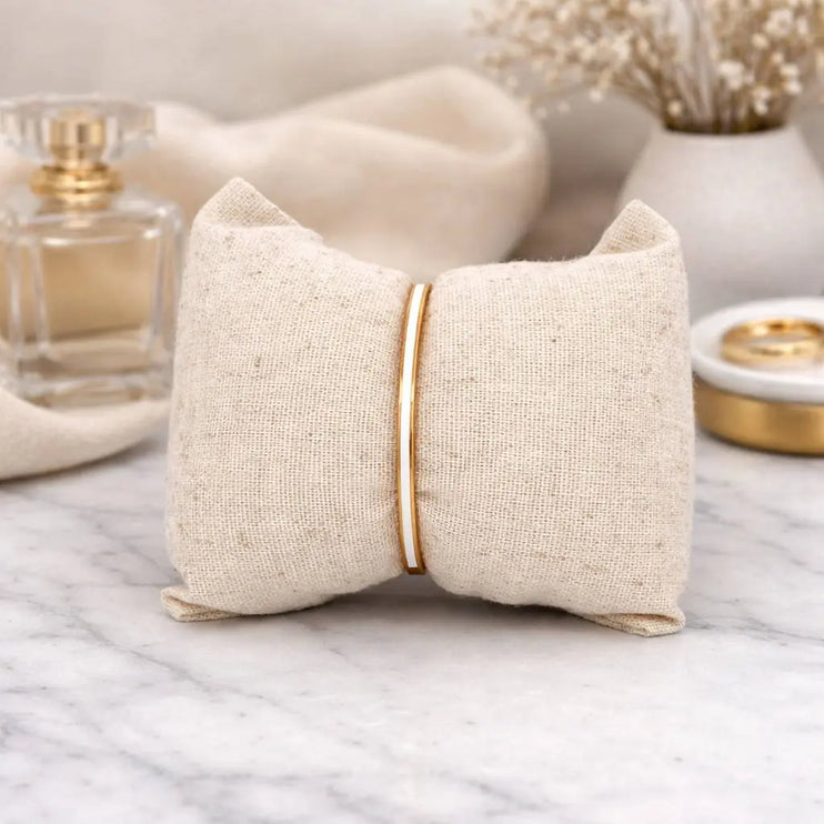 Beige jewelry pillow with gold band on a marble surface with decorative items.