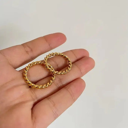 Gold hoop earrings held in a hand against a plain background