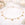 Gold necklace with heart pendants on a white surface with flowers and candles