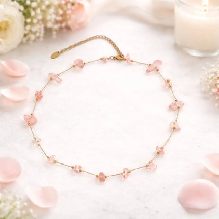 Necklace with pink beads on a white surface with flowers and petals.