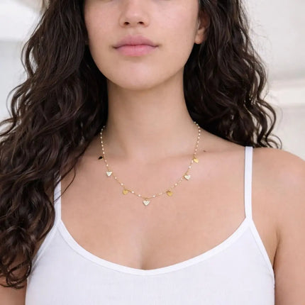 Woman wearing a delicate gold necklace with heart pendants against a neutral background