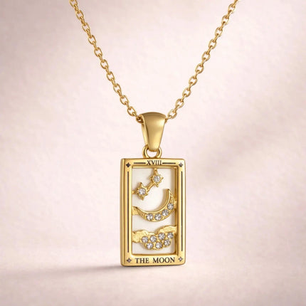 Gold pendant with 'The Moon' design on a chain against a light pink background