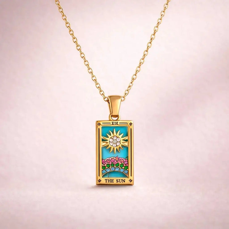 Gold pendant with 'The Sun' tarot card design on a pink background