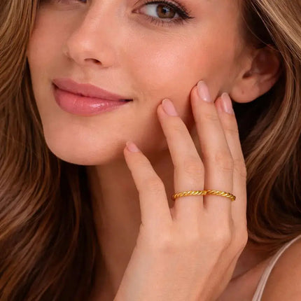 Woman wearing a gold ring on her finger, touching her face.